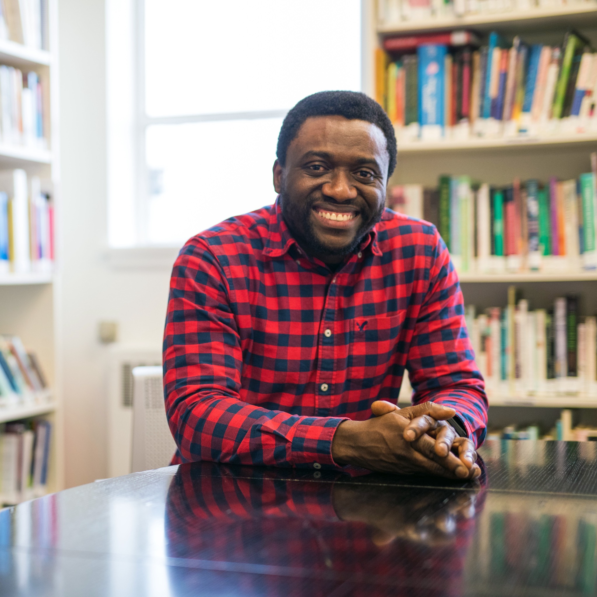 Portrait of Femi Ogunji smiling in front of bookshelves
